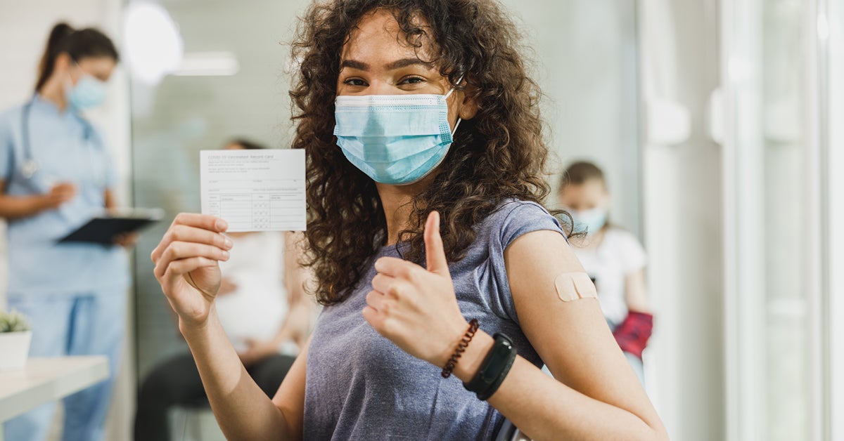 girl with mask on holding up her vaccintion card