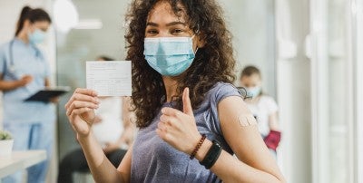girl with mask on holding up her vaccintion card