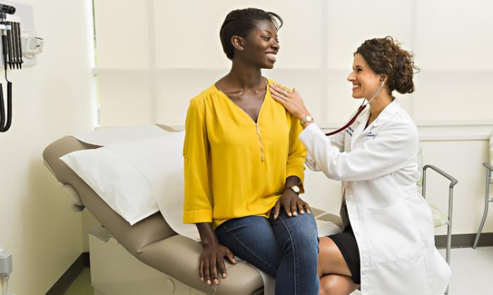 Smiling doctor uses stethoscope with smiling patient