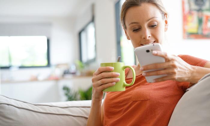 Woman on a sofa holding a mug and looking at a smart phone