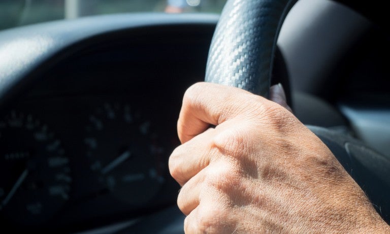 Hand on steering wheel in car.